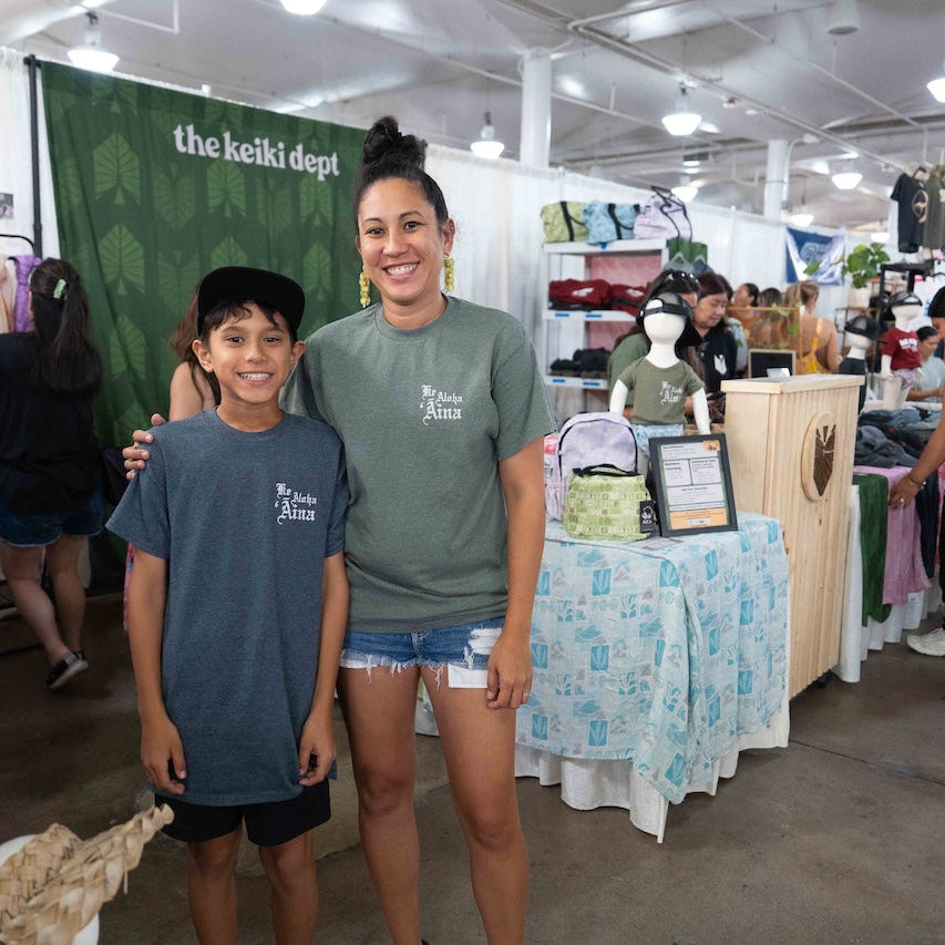 Two people standing together at a market stall with 'the keiki dept' branding.