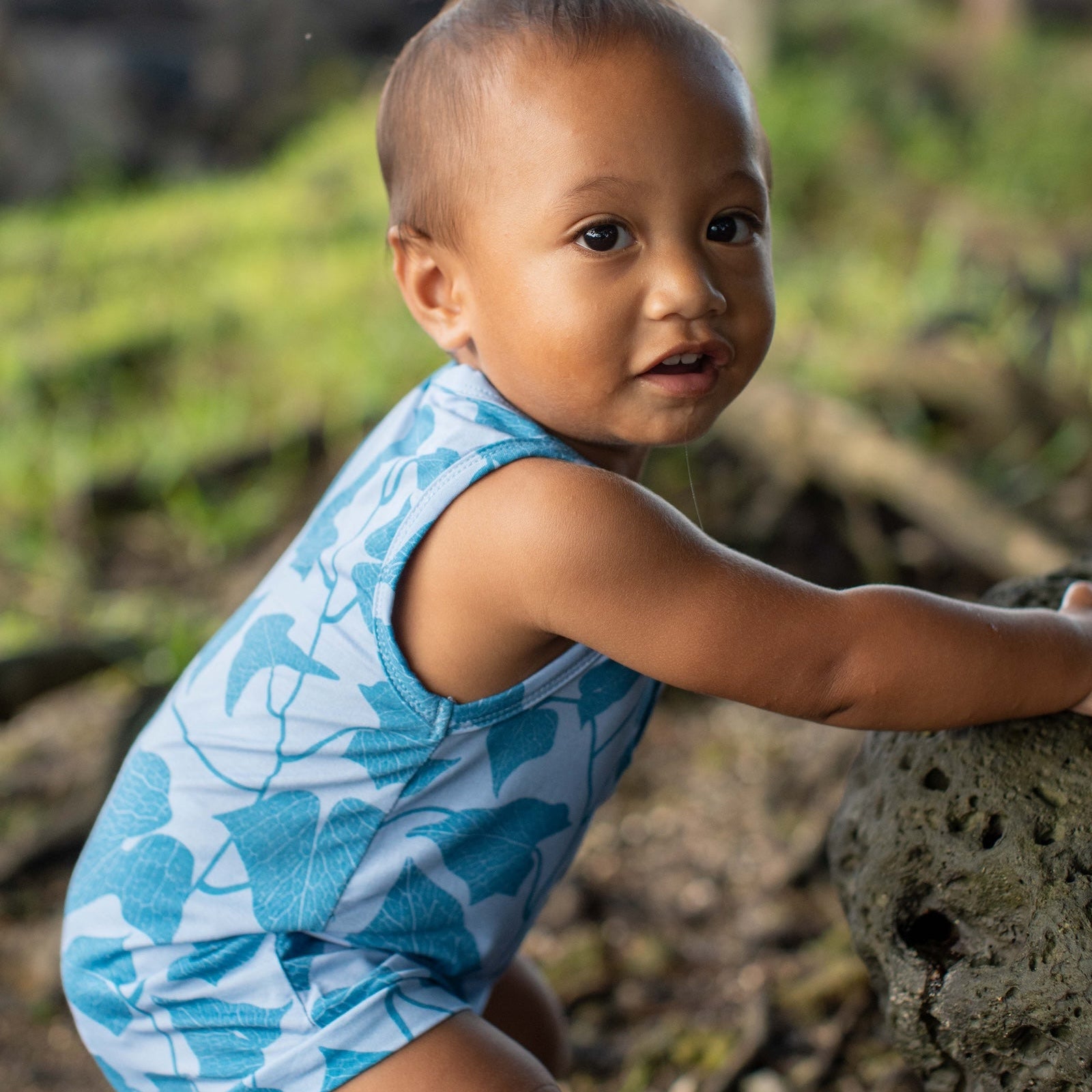 Child wearing a blue peahi fern patterned romper outdoors.