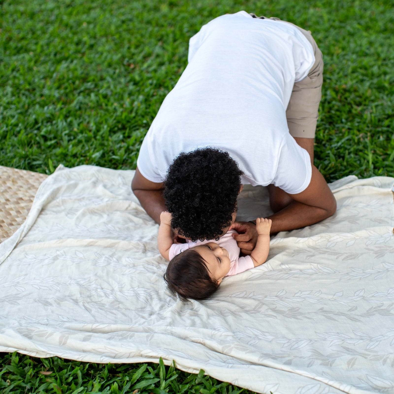 dad playing with his baby on blanket outdoors in a grassy areaa