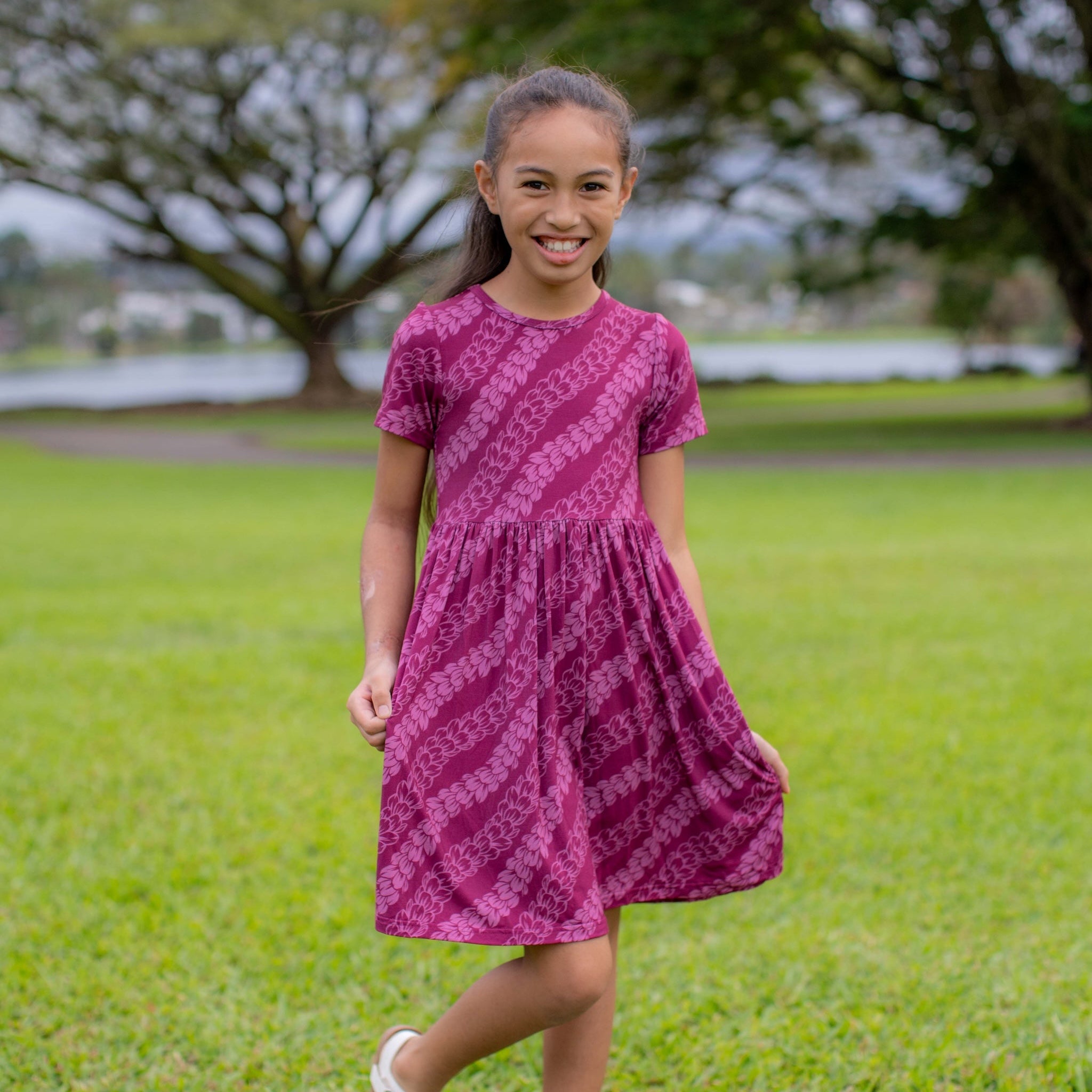 Young girl in a pakalana dress standing on grass with trees in the background