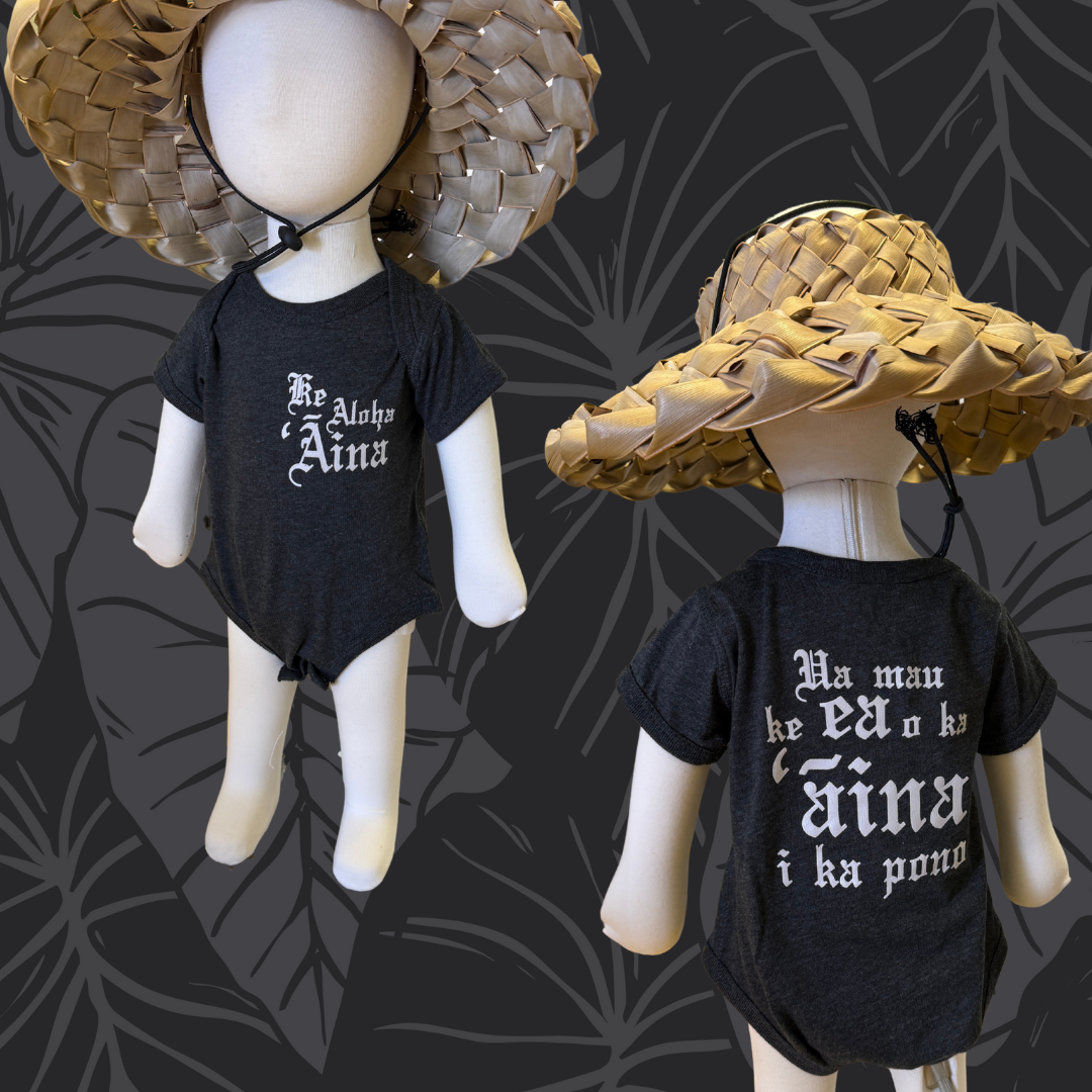 Two mannequins wearing black shirts with white text and straw hats on a dark leaf-patterned background.