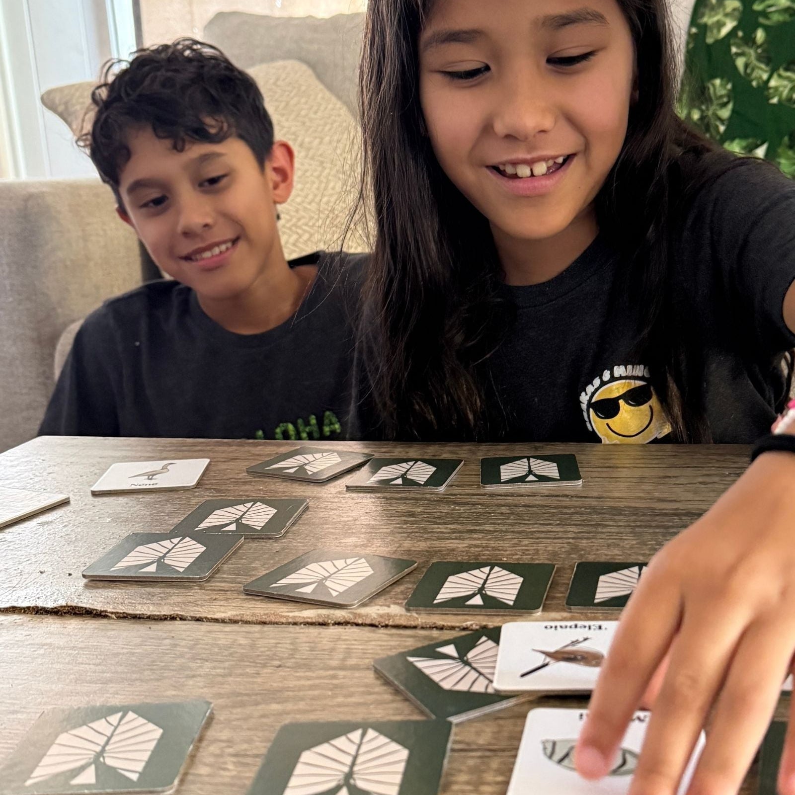 Two children playing a card game with cards on a wooden table.