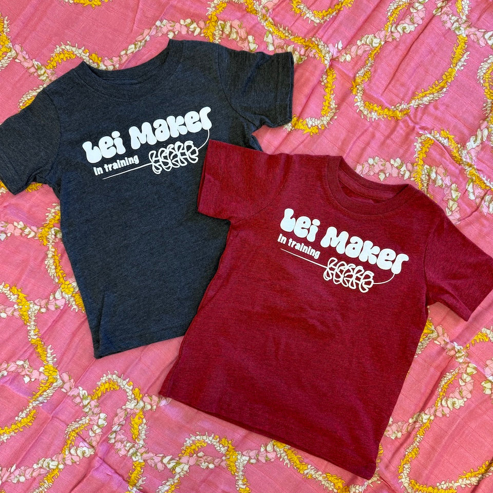 Two t-shirts, one black and one red, with 'Leli Maker in training' text on a pink lei patterned background.