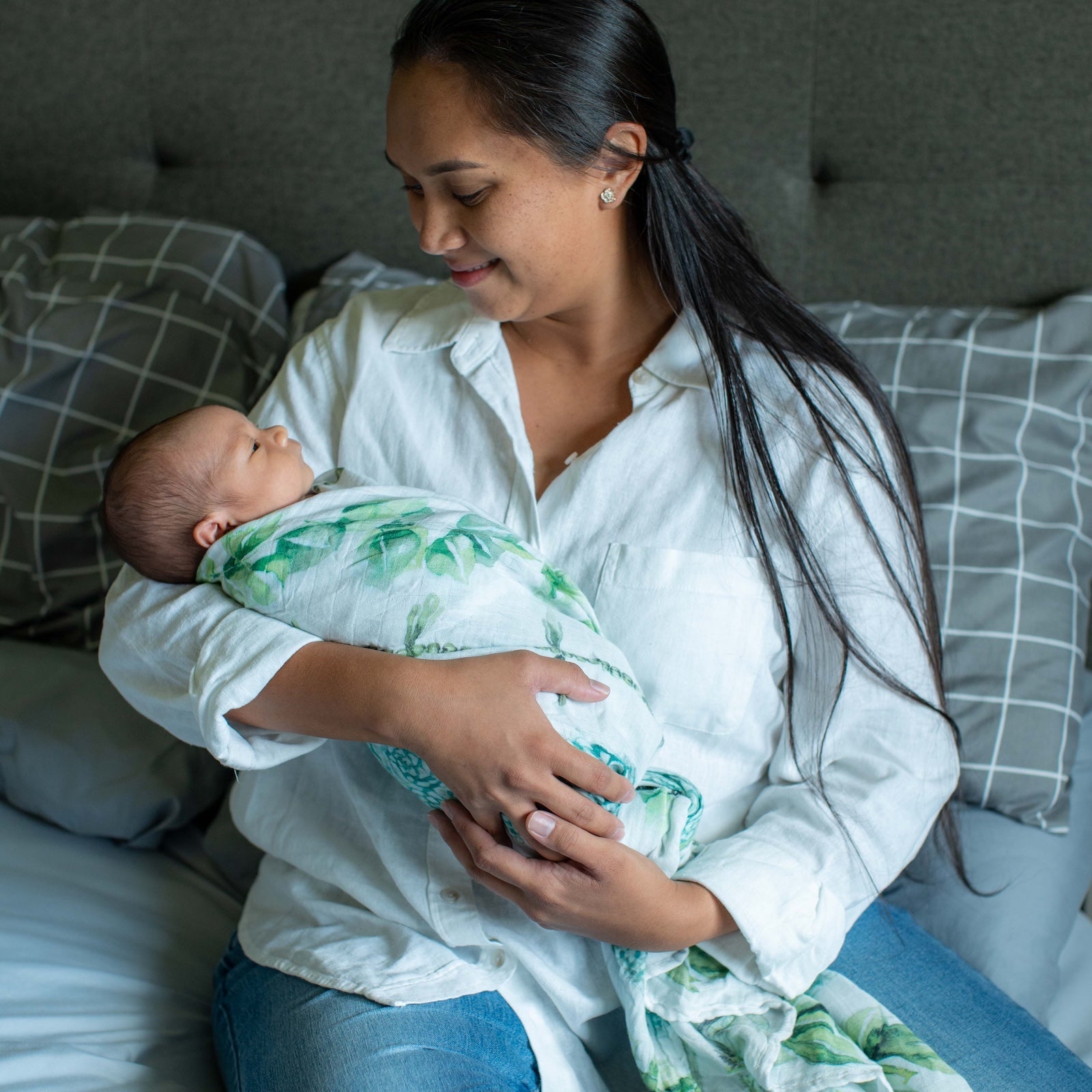 Woman holding a baby wrapped in a green blanket on a bed.
