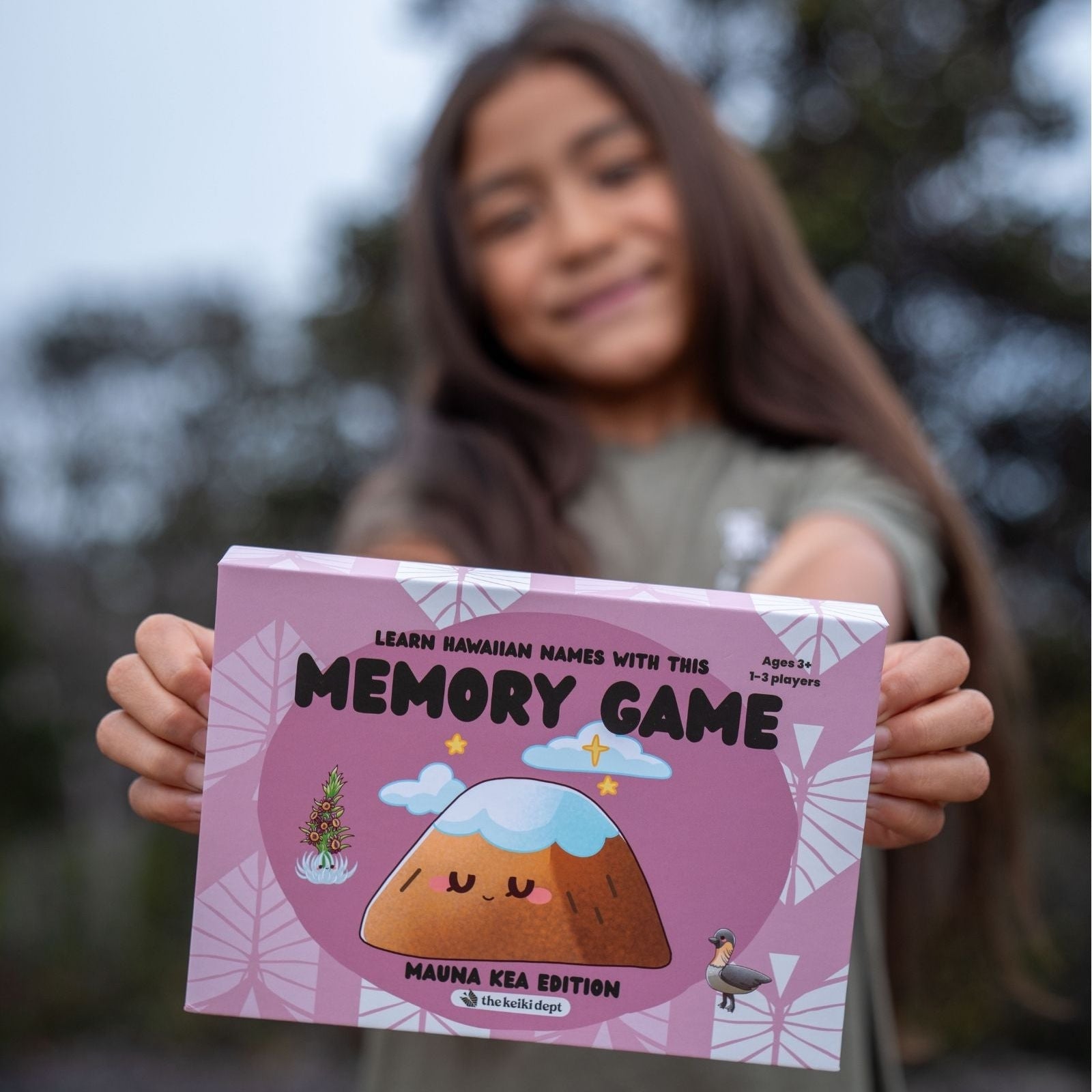girl holding a pink memory game box with a blurred outdoor background