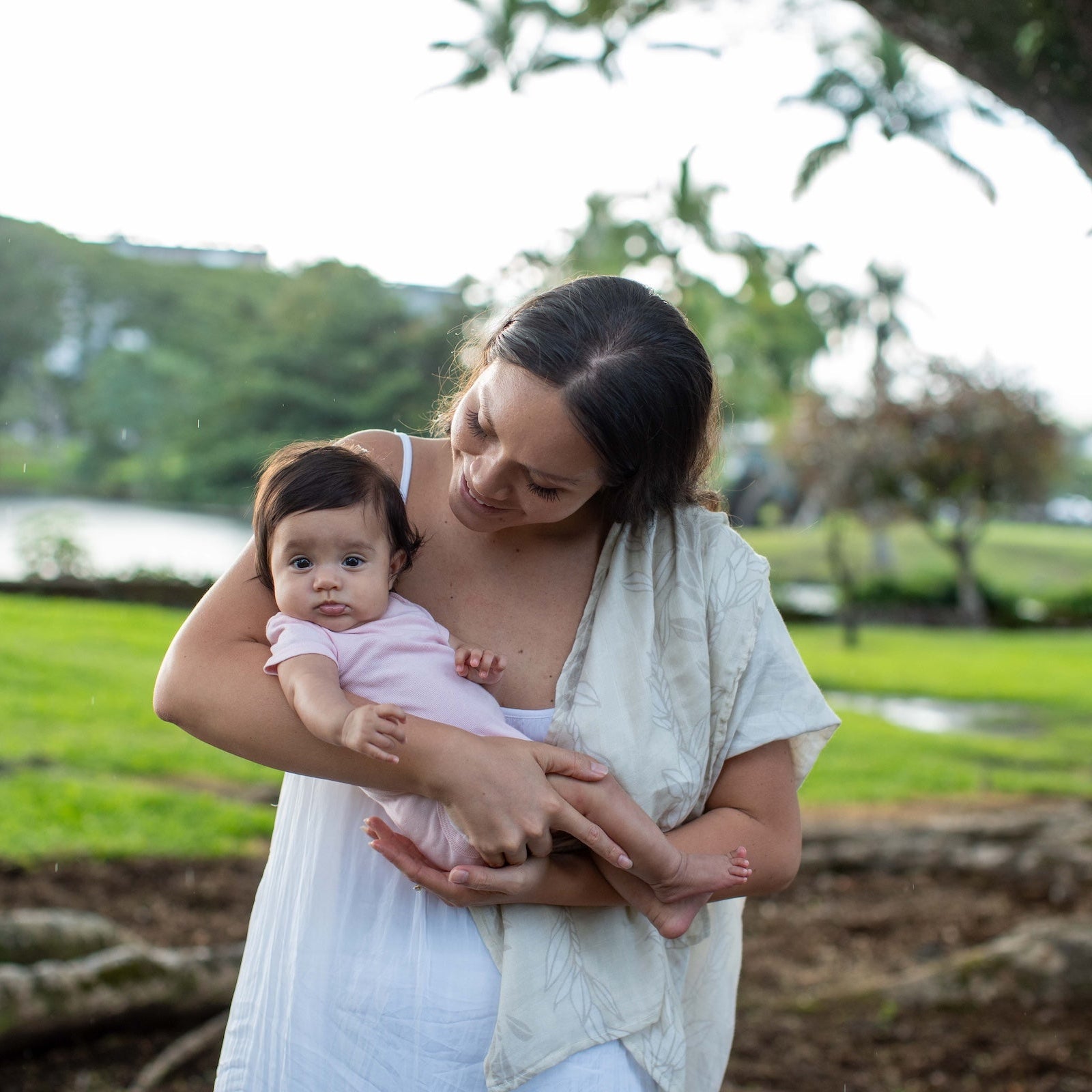 Woman holding a baby outdoors with greenery in the background