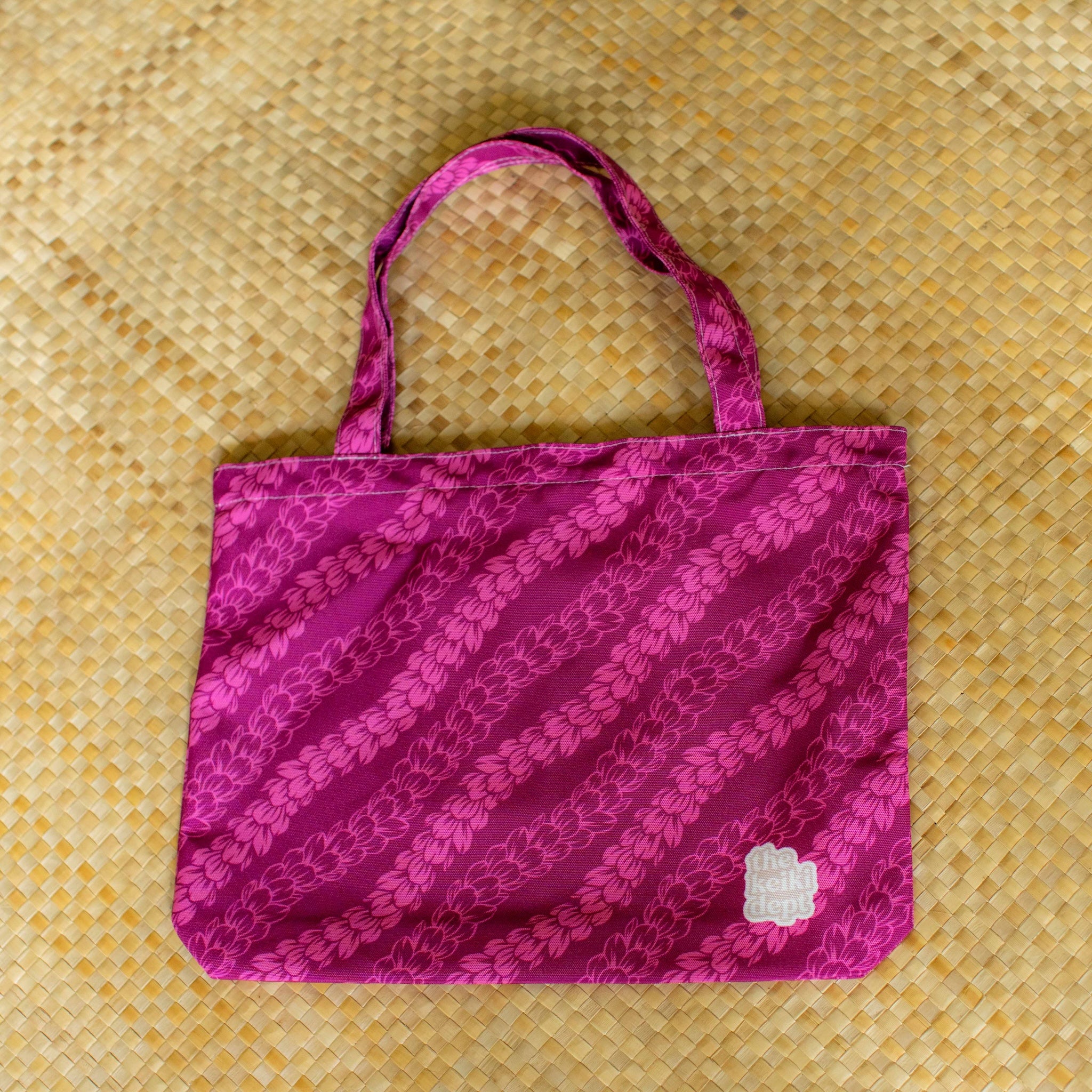 magenta pink canvas tote bag with pakalana flower lei strands on a lauhala mat