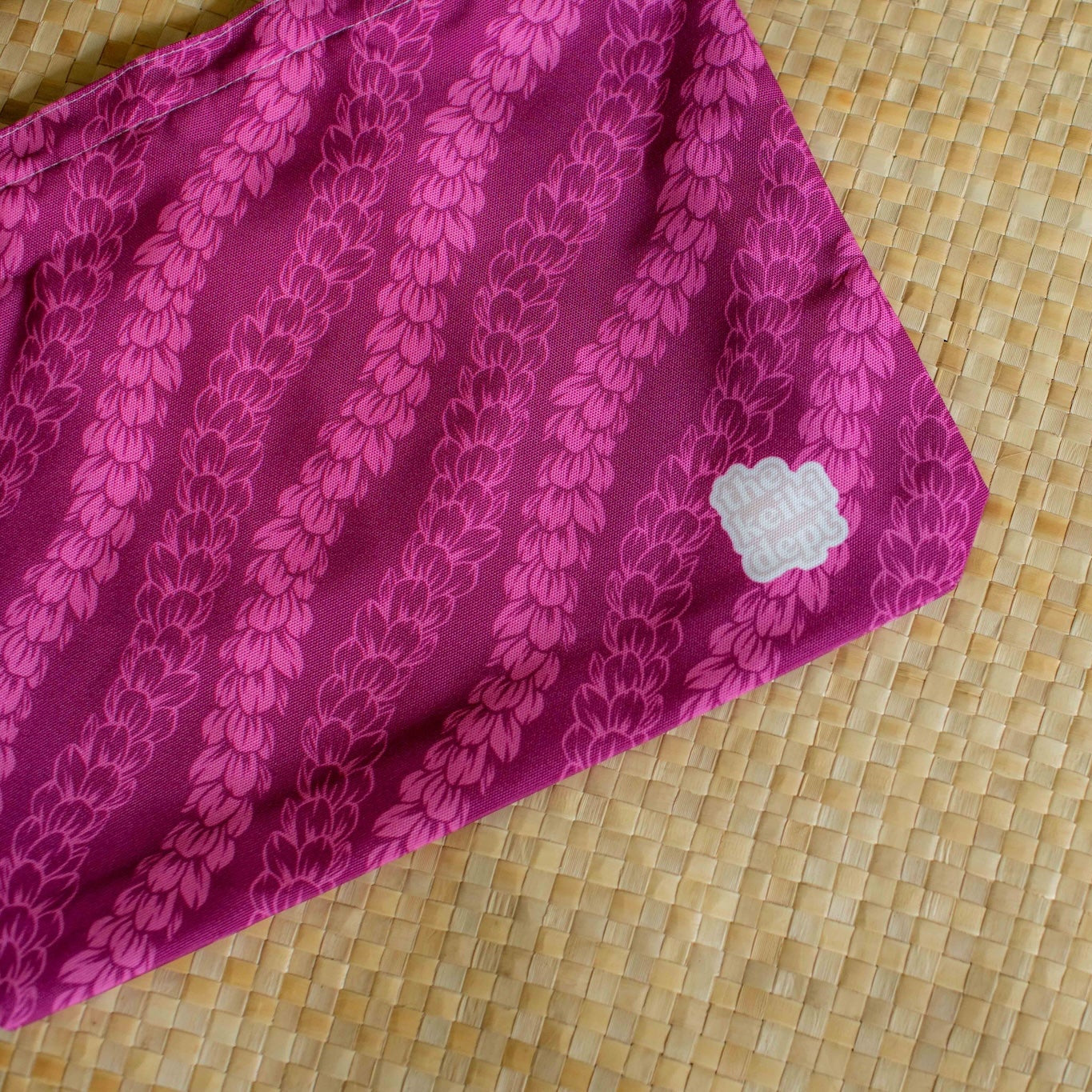 magenta pink canvas tote bag with pakalana flower lei strands on a lauhala mat