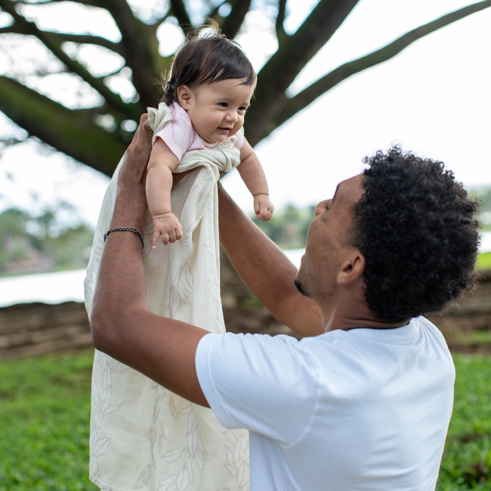 Man holding a baby in a natural outdoor setting with trees and grass.