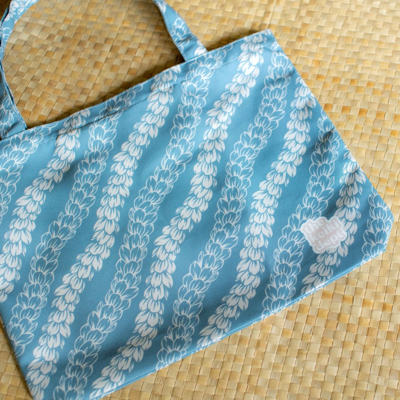 Blue fabric bag with white pakalana flower lei on a lauhala mat
