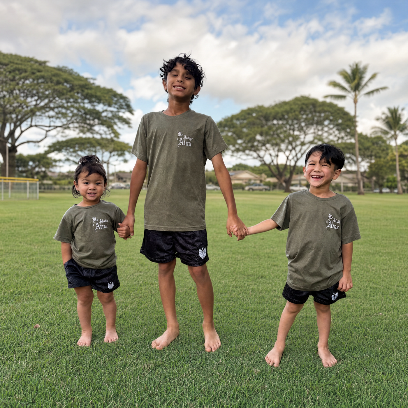 Three children holding hands on a grassy field with trees and a cloudy sky in the background.