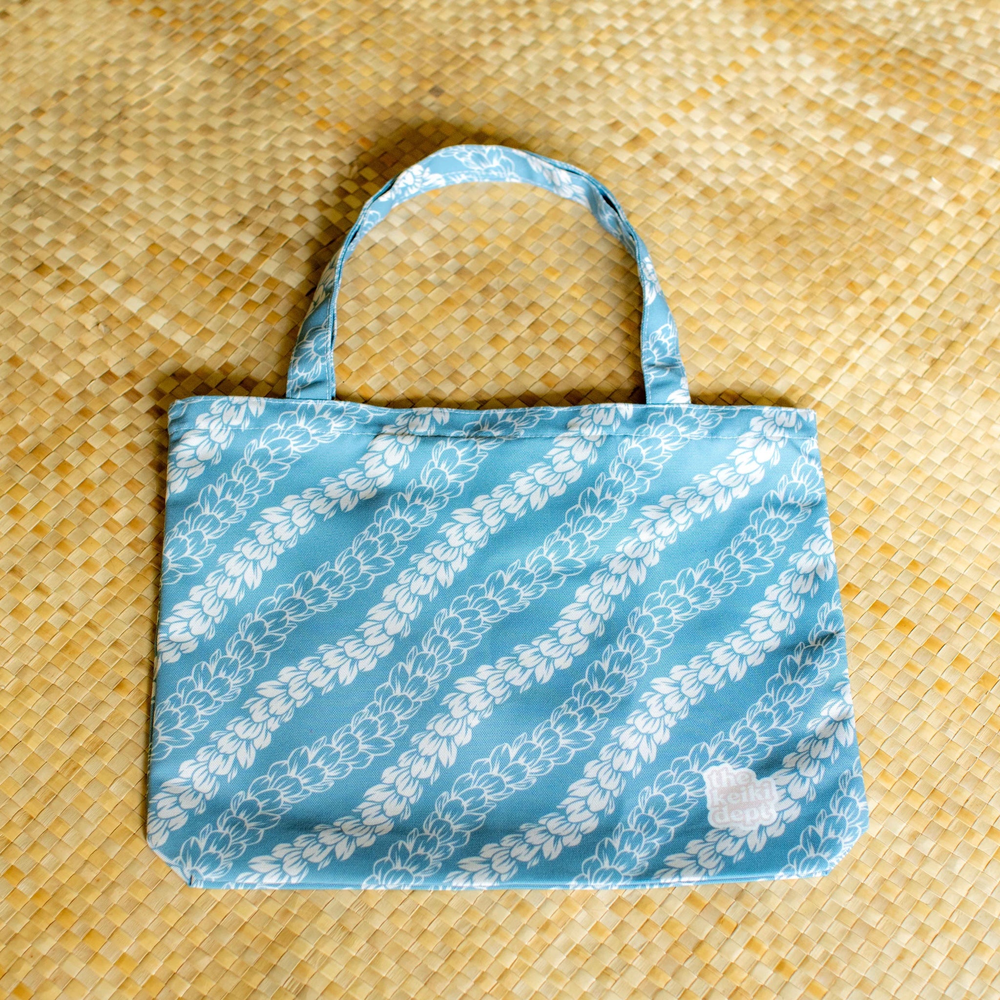 Blue tote bag with white pakalana lei pattern on a lauhala mat
