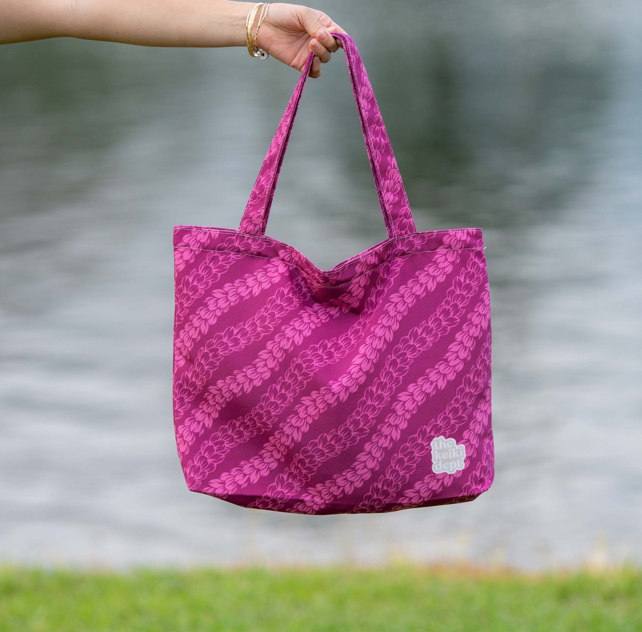 Person holding a magenta pink pakalana lei tote bag with a blurred natural background