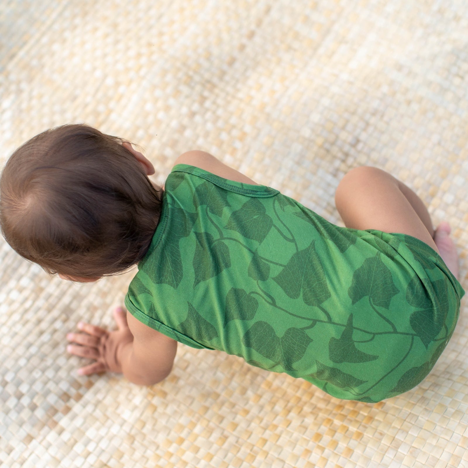 Baby in a green leaf-patterned onesie crawling on a textured surface