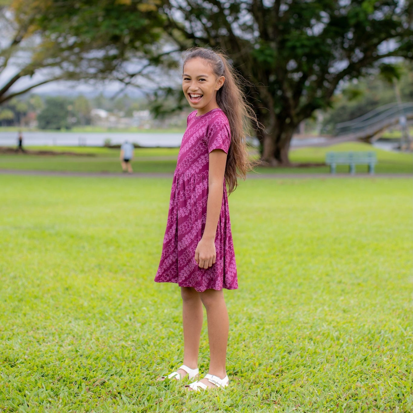 Young girl in a pakalana dress standing on grass with trees in the background