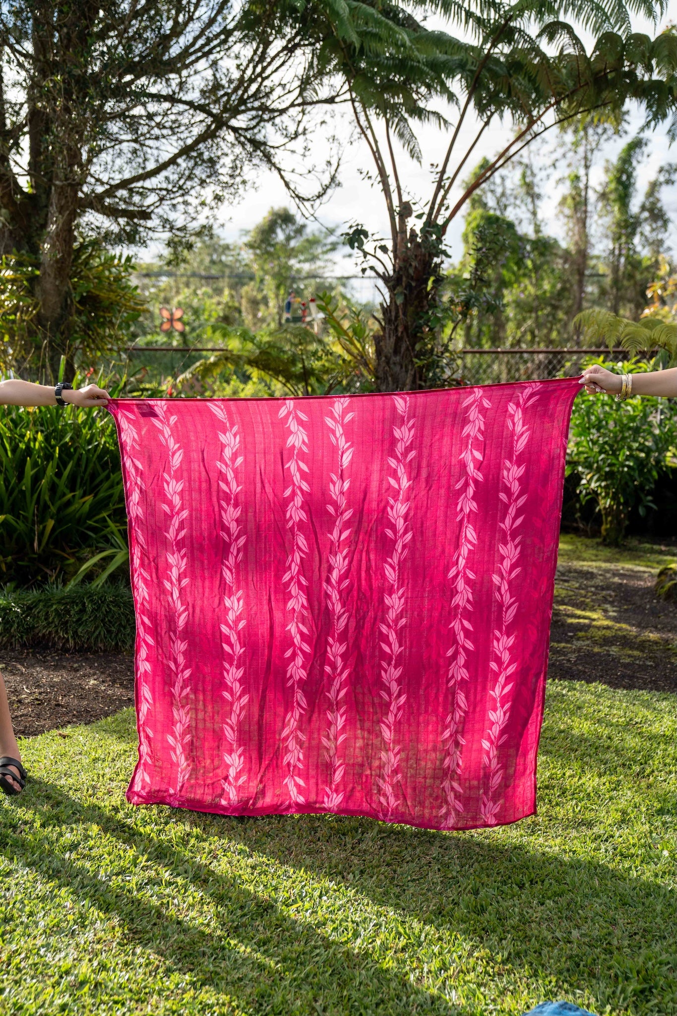 magenta pink pakalana strands fabric held up outdoors with greenery in the background