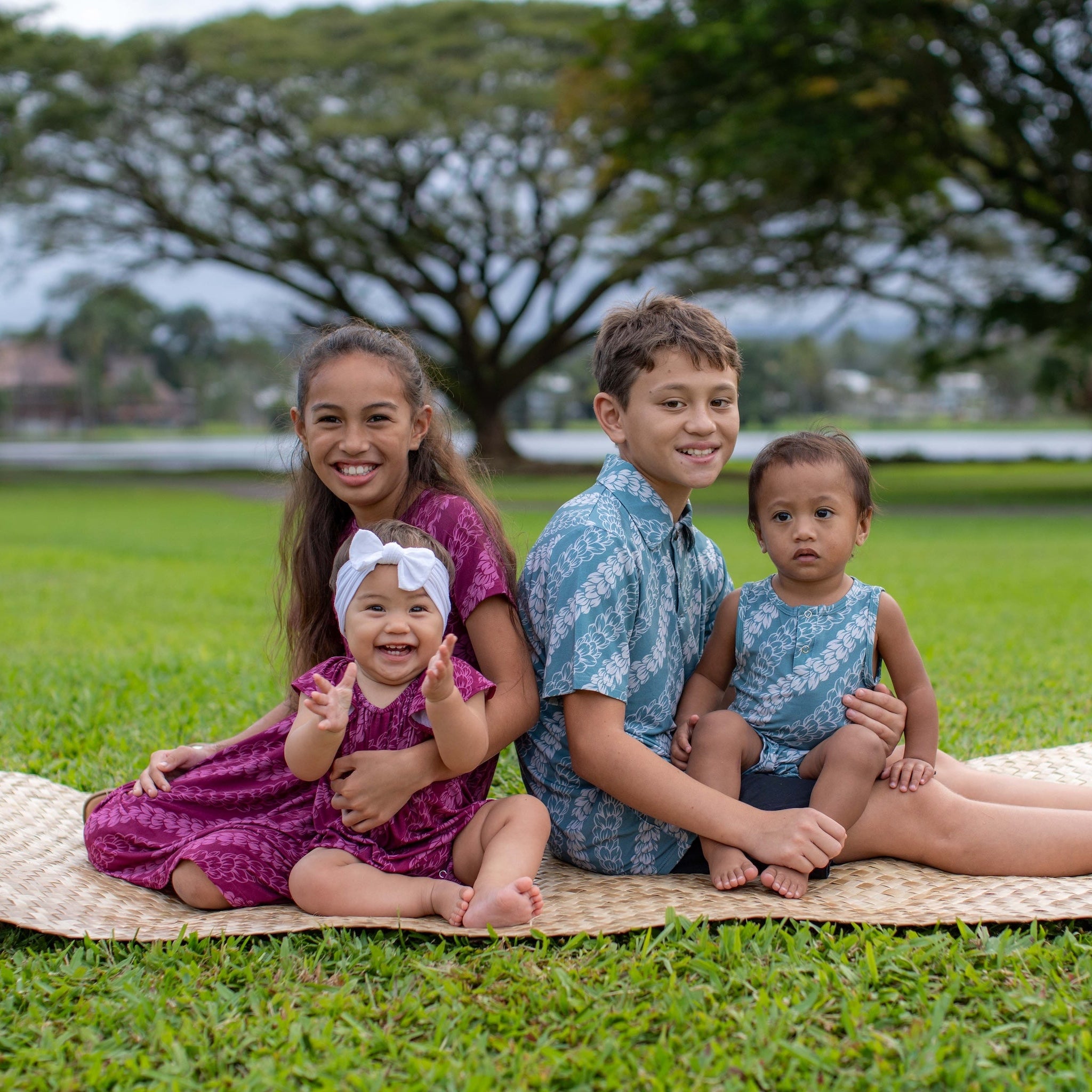 Four children wearing pakalana strands collection sitting on a woven mat in a park