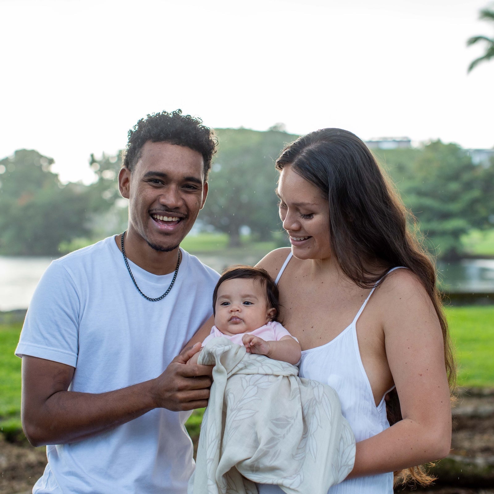 Family of three outdoors with water and greenery in the background