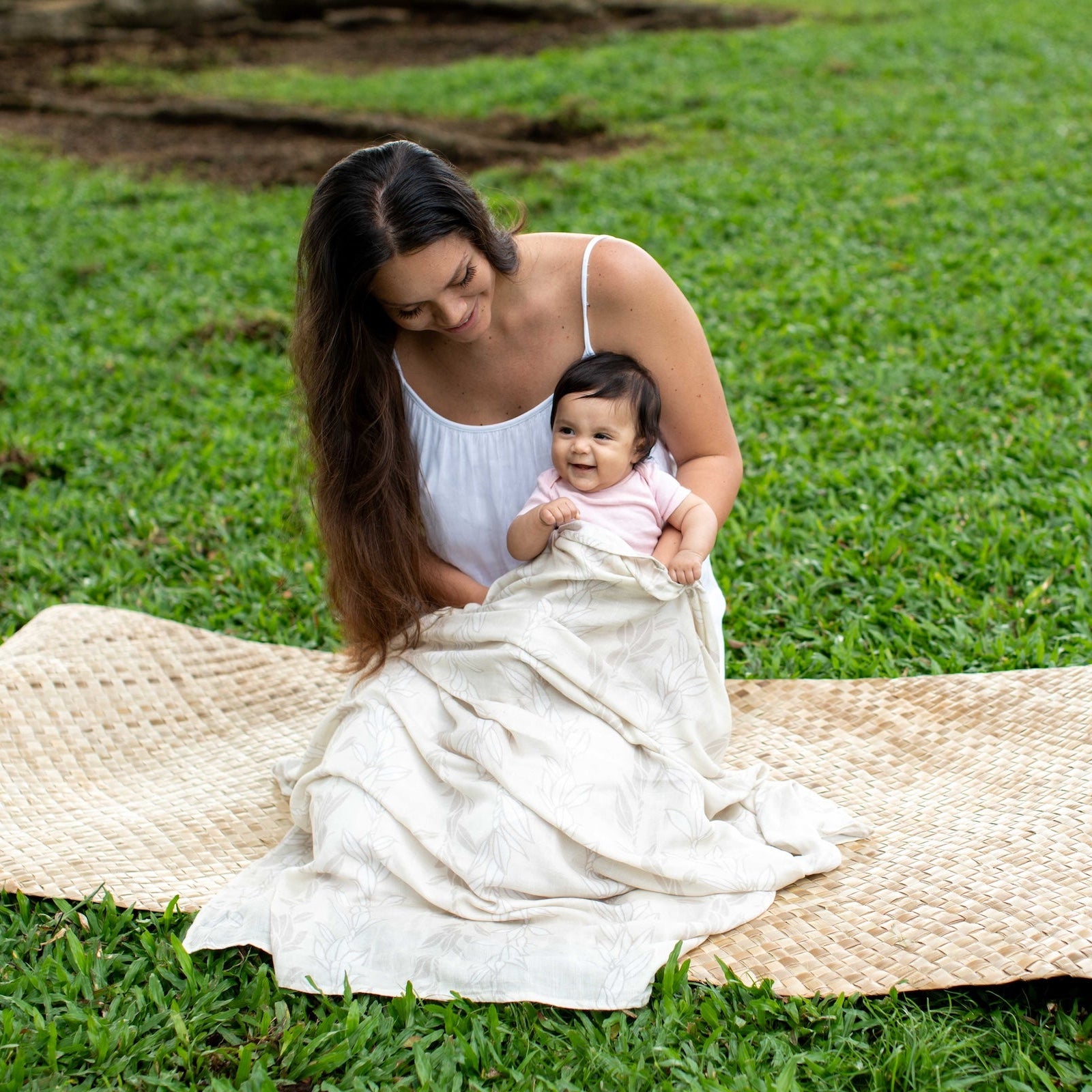 Woman holding a baby wrapped in a white blanket on a grassy field